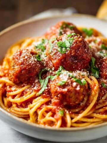 Spaghetti and Meatballs topped with meatballs in rich tomato sauce, sprinkled with Parmesan and fresh parsley.