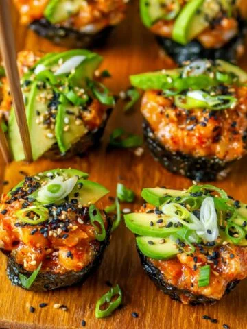 Baked Salmon Sushi Cups Recipe topped with avocado, green onions, sesame seeds, and spicy sauce, served on a plate with chopsticks.