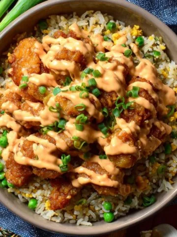Bang bang chicken fried rice topped with crispy chicken, creamy sauce, peas, and green onions.