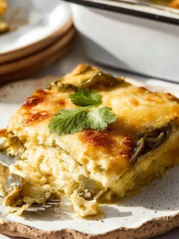 Slice of homemade chile relleno casserole on a rustic plate with melted cheese, roasted chiles, and a forkful taken out.