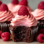 Chocolate Raspberry Cupcakes and a fresh raspberry on top, with a bite taken out showing the moist cake inside.