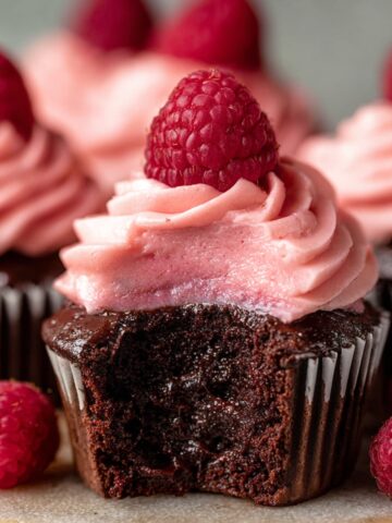 Chocolate Raspberry Cupcakes and a fresh raspberry on top, with a bite taken out showing the moist cake inside.