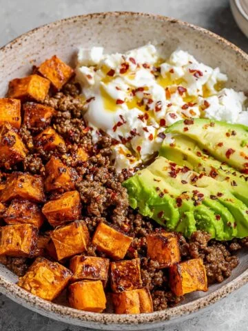 A serving of Cottage Cheese Taco Bowl with roasted sweet potatoes, ground beef, avocado slices, and a sprinkle of chili flakes.