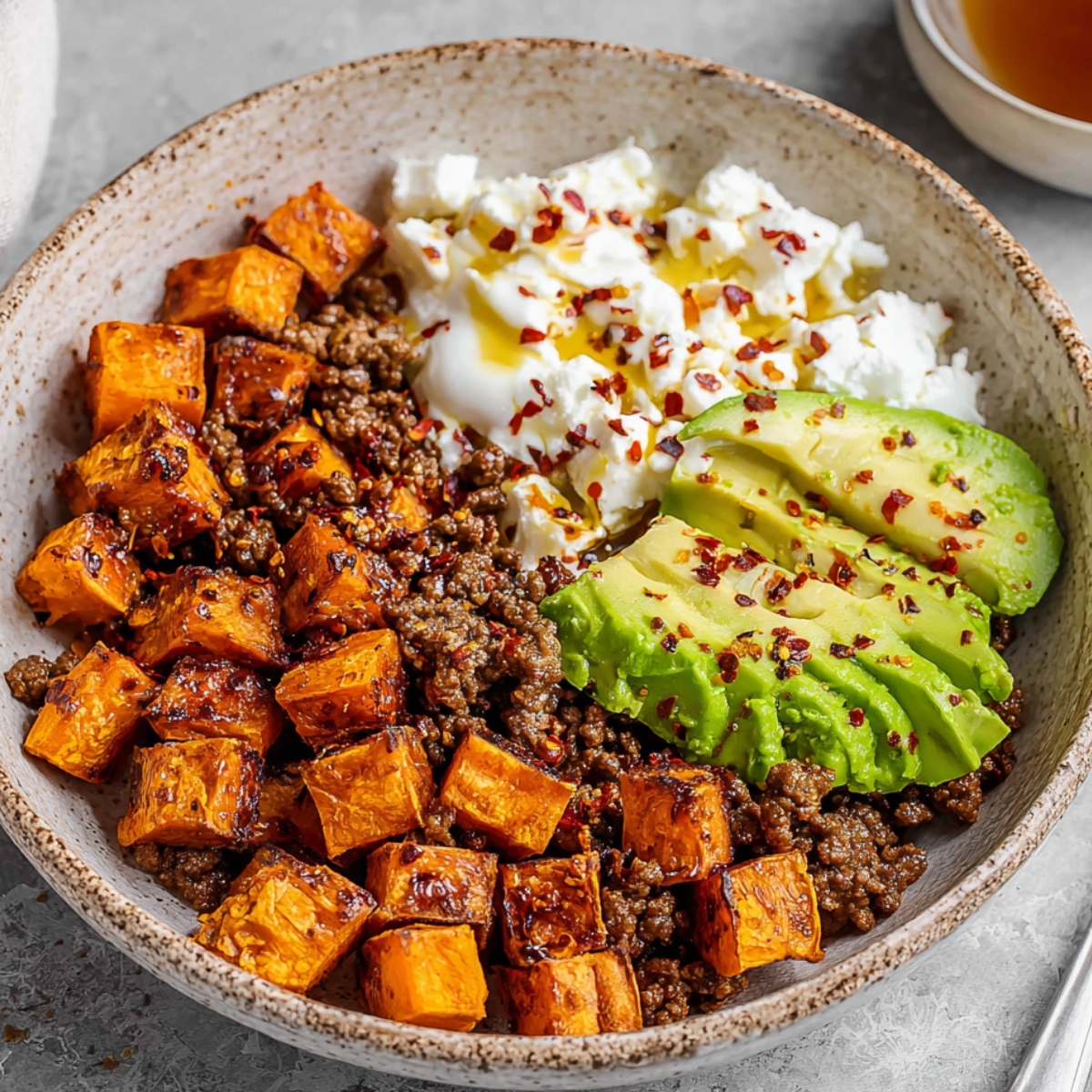 A serving of Cottage Cheese Taco Bowl with roasted sweet potatoes, ground beef, avocado slices, and a sprinkle of chili flakes.