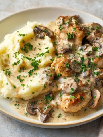 A plate of creamy chicken stroganoff with sautéed mushrooms, served alongside mashed potatoes, garnished with fresh parsley.