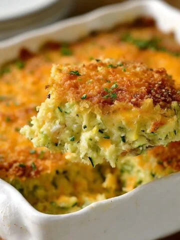 Slice of homemade cheesy zucchini casserole on a plate, showing a golden, crispy breadcrumb topping and tender zucchini filling.