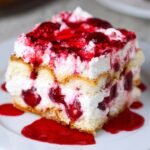 Homemade Cherry Amaretto Tiramisu with whipped cream, cherries, and cherry syrup on top, served on a white plate.