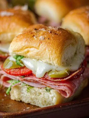 Hot Italian Sub Sliders with melted cheese, sliced meats, peppers, and fresh herbs on toasted golden rolls.