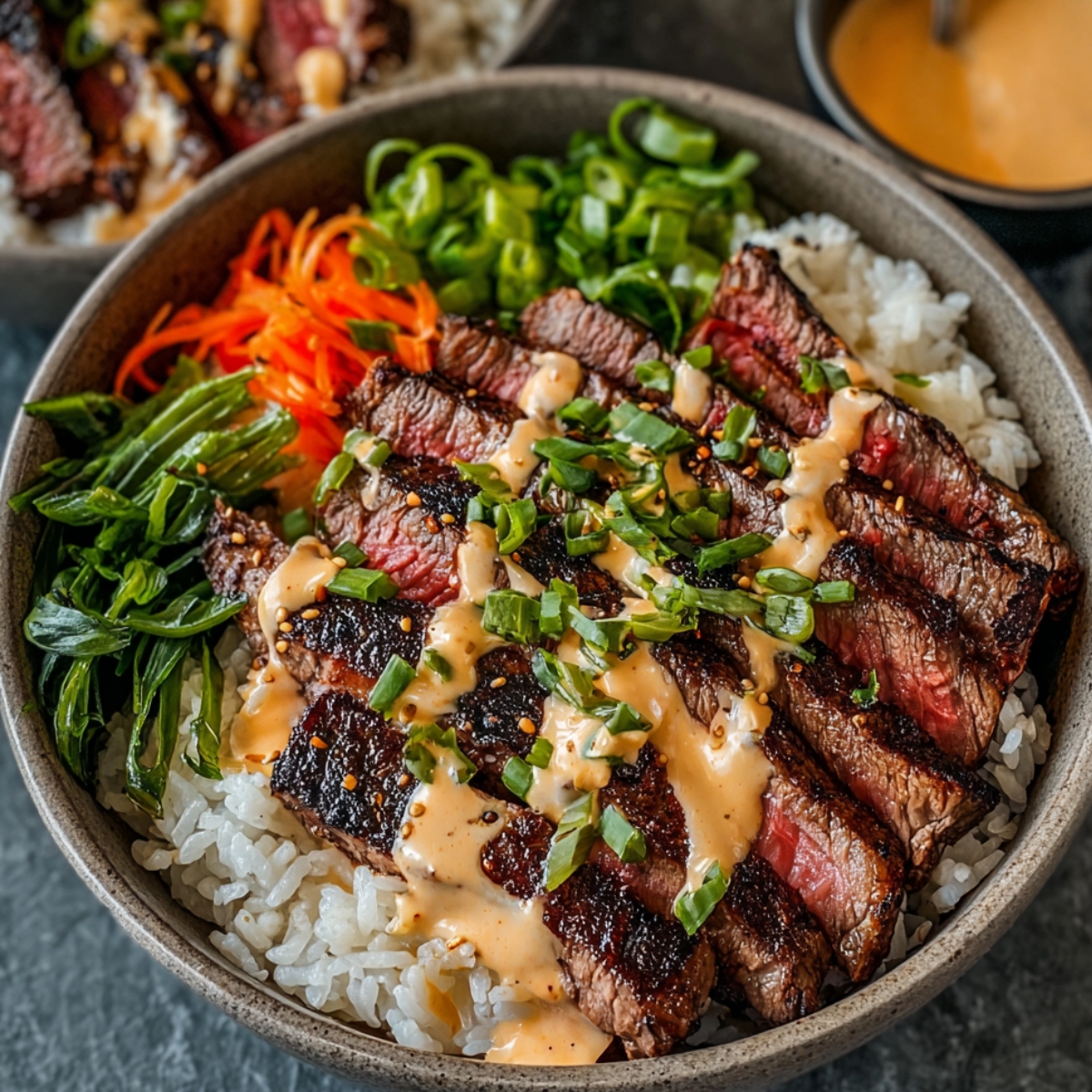 Korean BBQ Steak Bowls with Creamy Sauce with sliced grilled steak, rice, spicy mayo, green onions, and shredded vegetables.