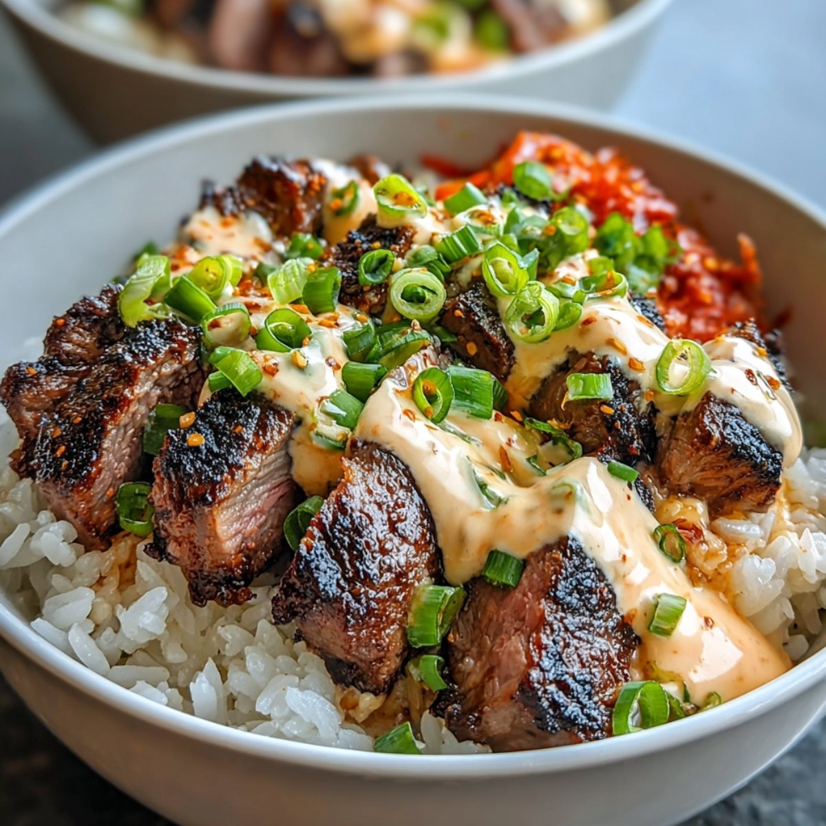 A homemade Korean BBQ Steak Bowls with grilled steak, rice, spicy mayo, scallions, and kimchi.