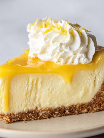 A slice of lemon cheesecake with a smooth interior, topped with lemon curd and whipped cream.
