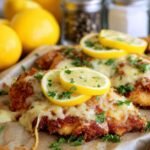Crispy homemade lemon chicken Romano topped with melted cheese, fresh lemon slices, and chopped parsley.