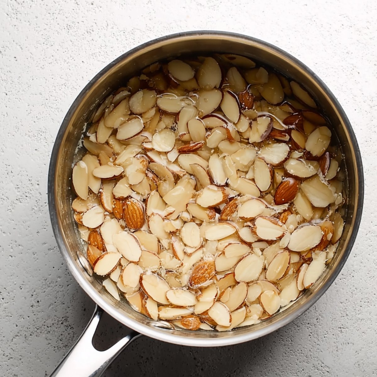 Combine the butter, honey, and sugar in a small heavy-bottomed saucepan over medium heat. Stir occasionally until the sugar dissolves and the mixture starts to bubble. It'll smell like caramel and honey mixed together. Remove it from the heat and stir in the sliced almonds until they're fully coated. Set it aside to cool while the dough finishes rising.