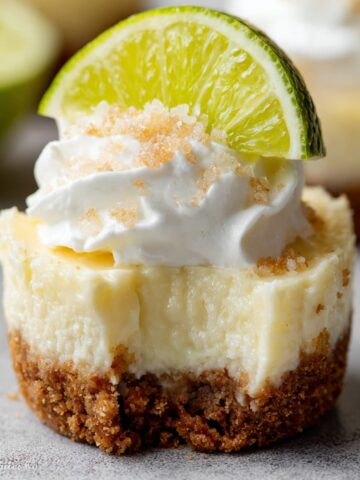 Mini Margarita Cheesecakes topped with whipped cream and a slice of lime, showcasing a smooth, creamy texture with a graham cracker crust.