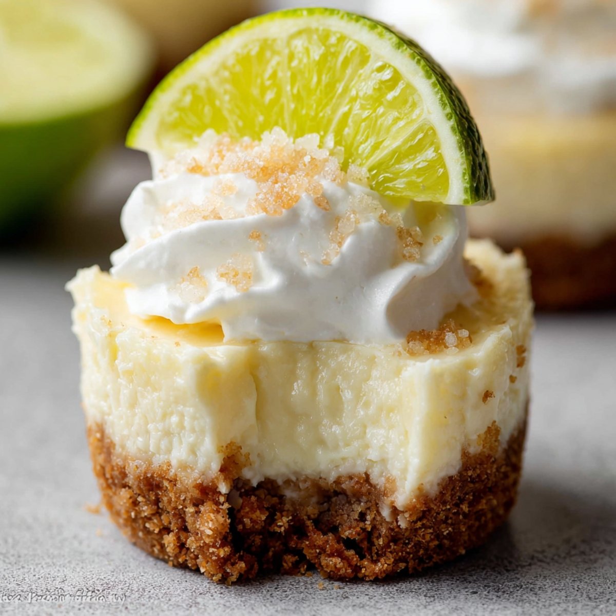 Mini Margarita Cheesecakes topped with whipped cream and a slice of lime, showcasing a smooth, creamy texture with a graham cracker crust.