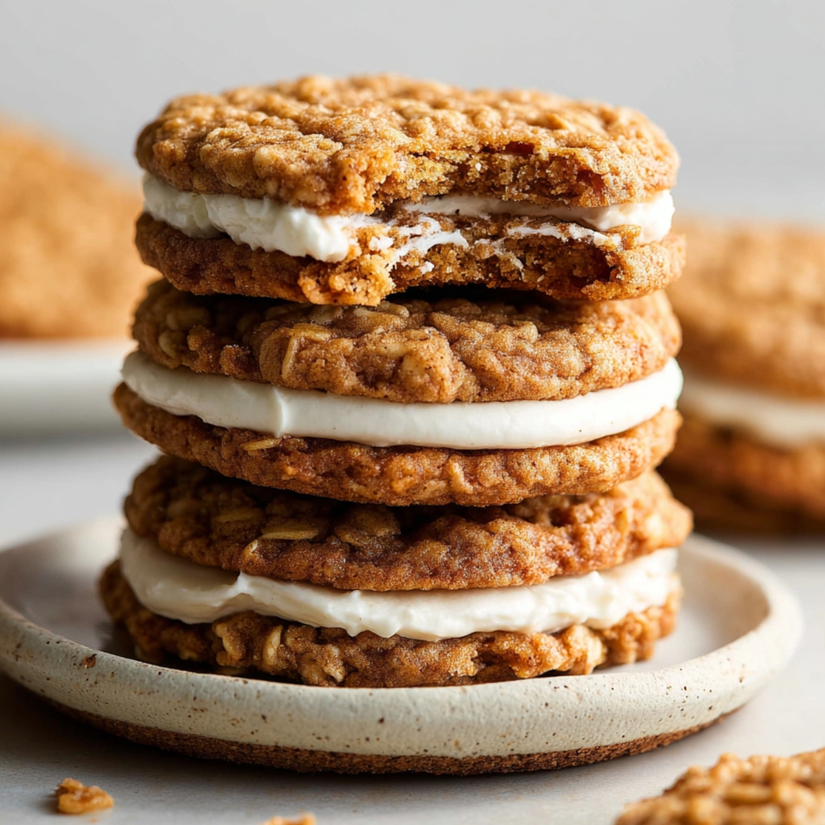 Oatmeal Cream Pies, with one showing a bite taken out, revealing the creamy filling between the oatmeal cookies. The cookies are golden brown and placed on a rustic plate.
