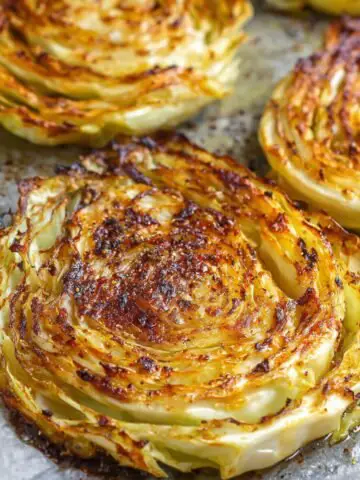 Roasted Cabbage Steaks Recipe with a crispy, caramelized texture. They are cut into thick slices and seasoned, giving them a beautiful golden-brown color.