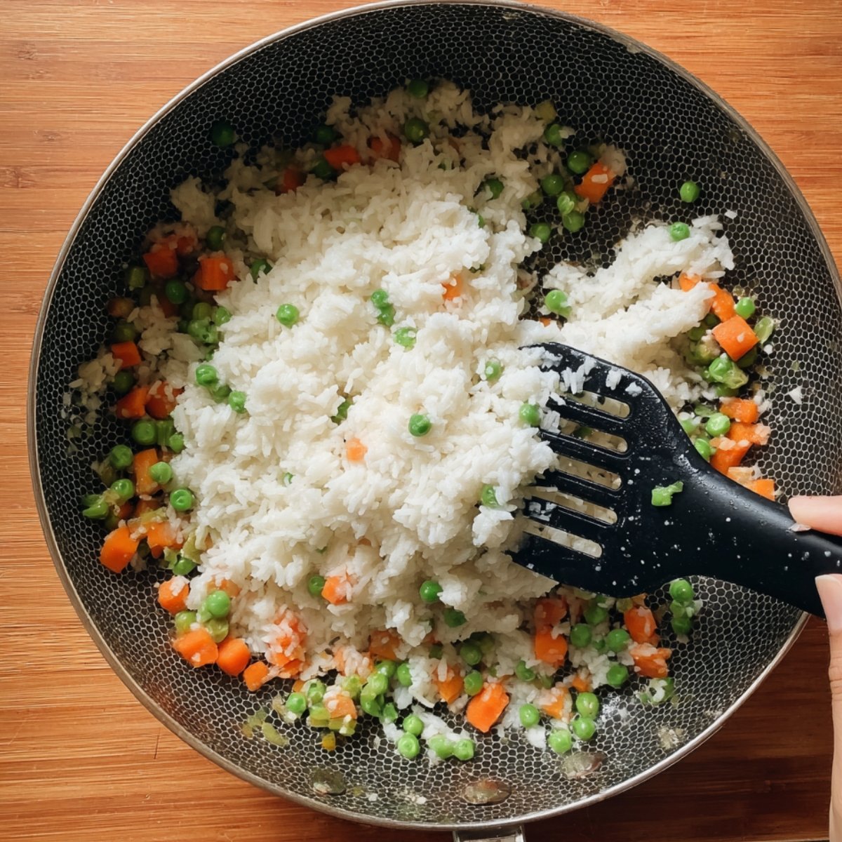 Add the day-old rice to the pan, breaking up any clumps with your spatula. Pour in the sesame oil and soy sauce, stirring everything together so the rice gets coated and starts to toast slightly. Push the rice to one side of the pan, crack the eggs into the empty space, and scramble them until they're just cooked. Then mix the eggs into the rice so you get little pieces throughout.
