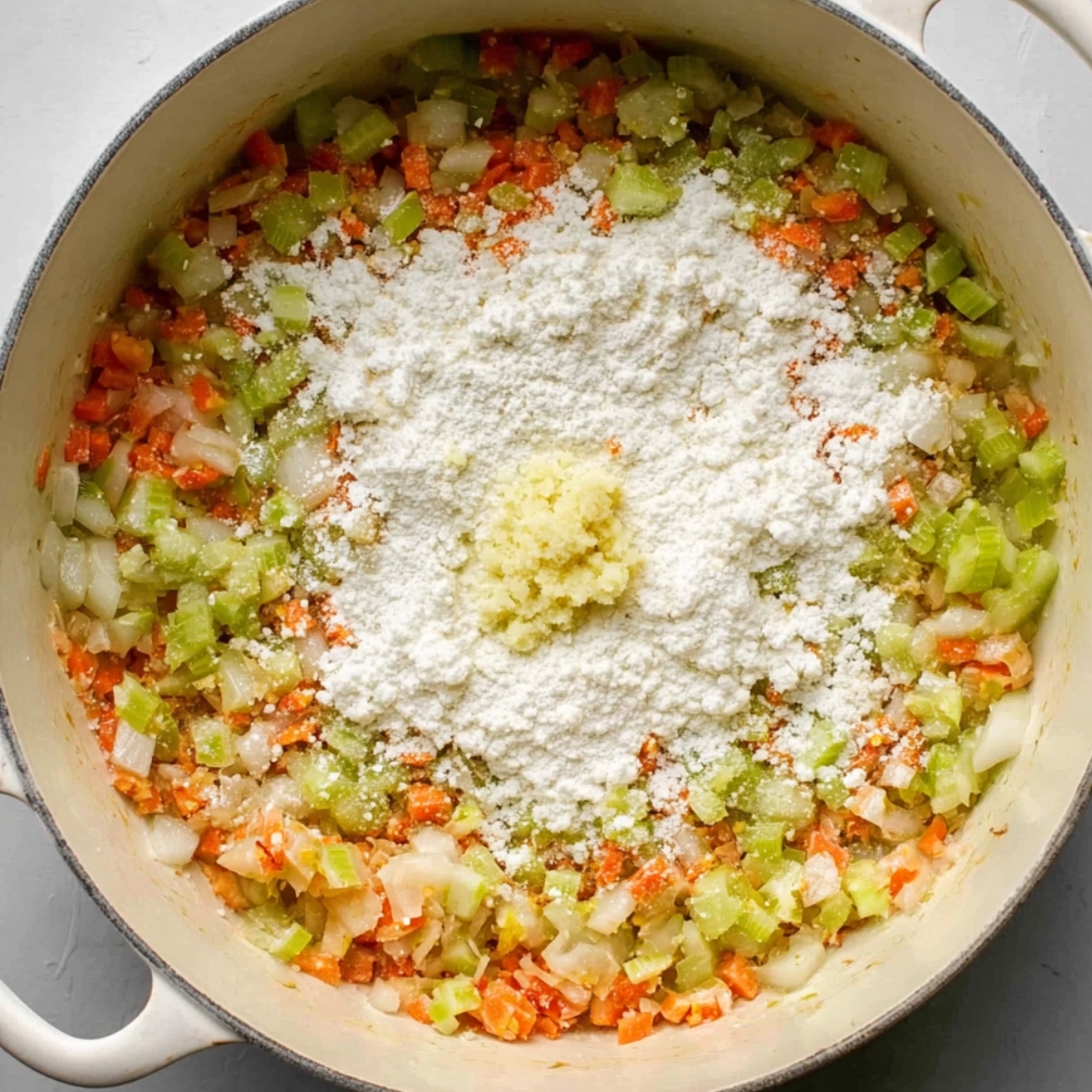 Flour and minced garlic added to sautéed celery, carrots, and onions in a pot to make a roux for soup