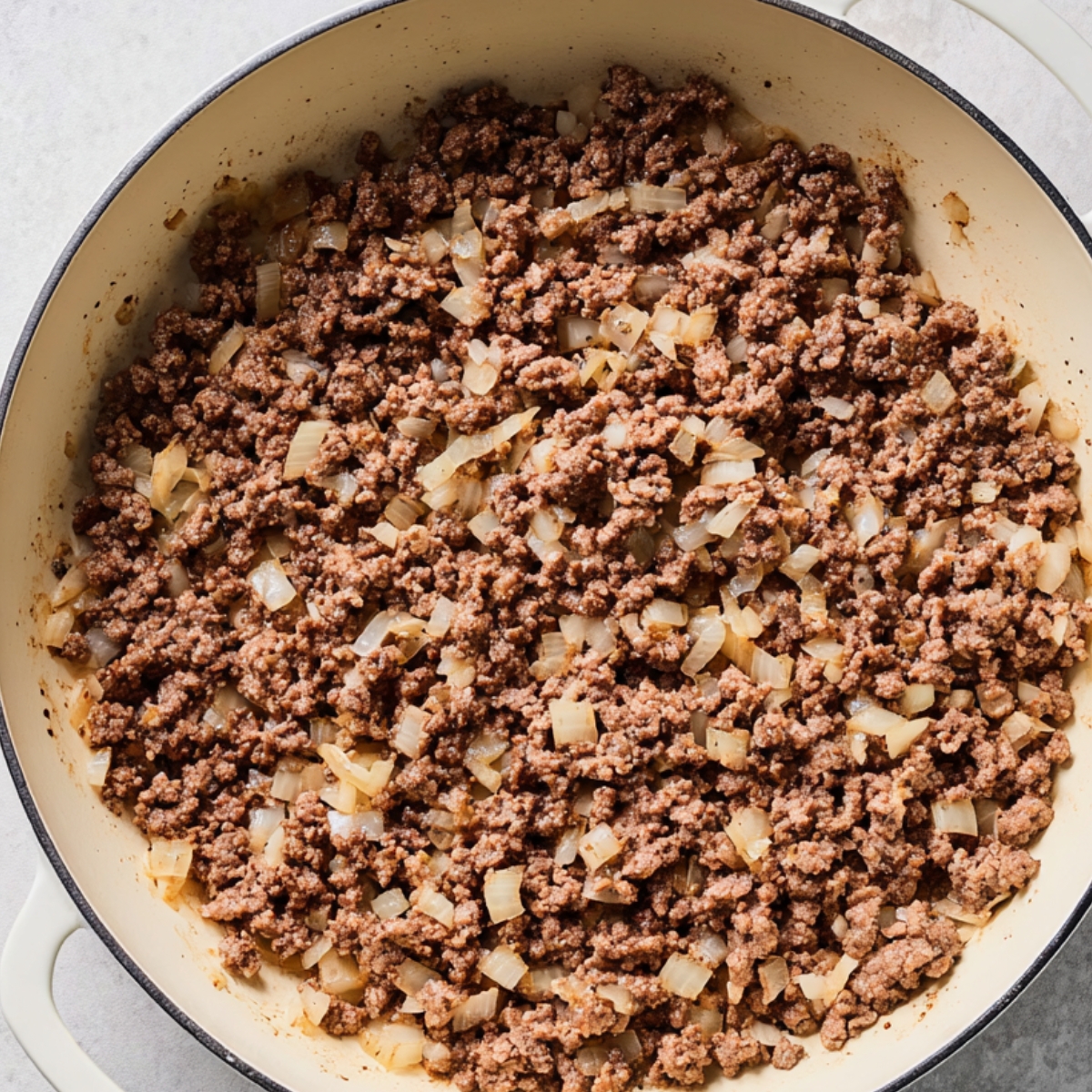 Ground beef and chopped onions cooking together in a large skillet