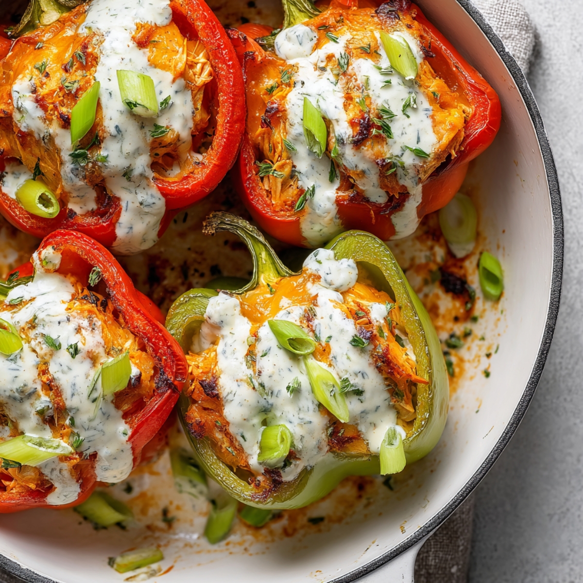 Close-up view of Buffalo Chicken Stuffed Peppers with creamy sauce and garnished with sliced green onions and herbs, showing melted, slightly charred edges.