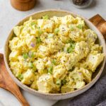 A creamy and freshly made classic potato salad, garnished with freshly ground black pepper and served in a light gray bowl.