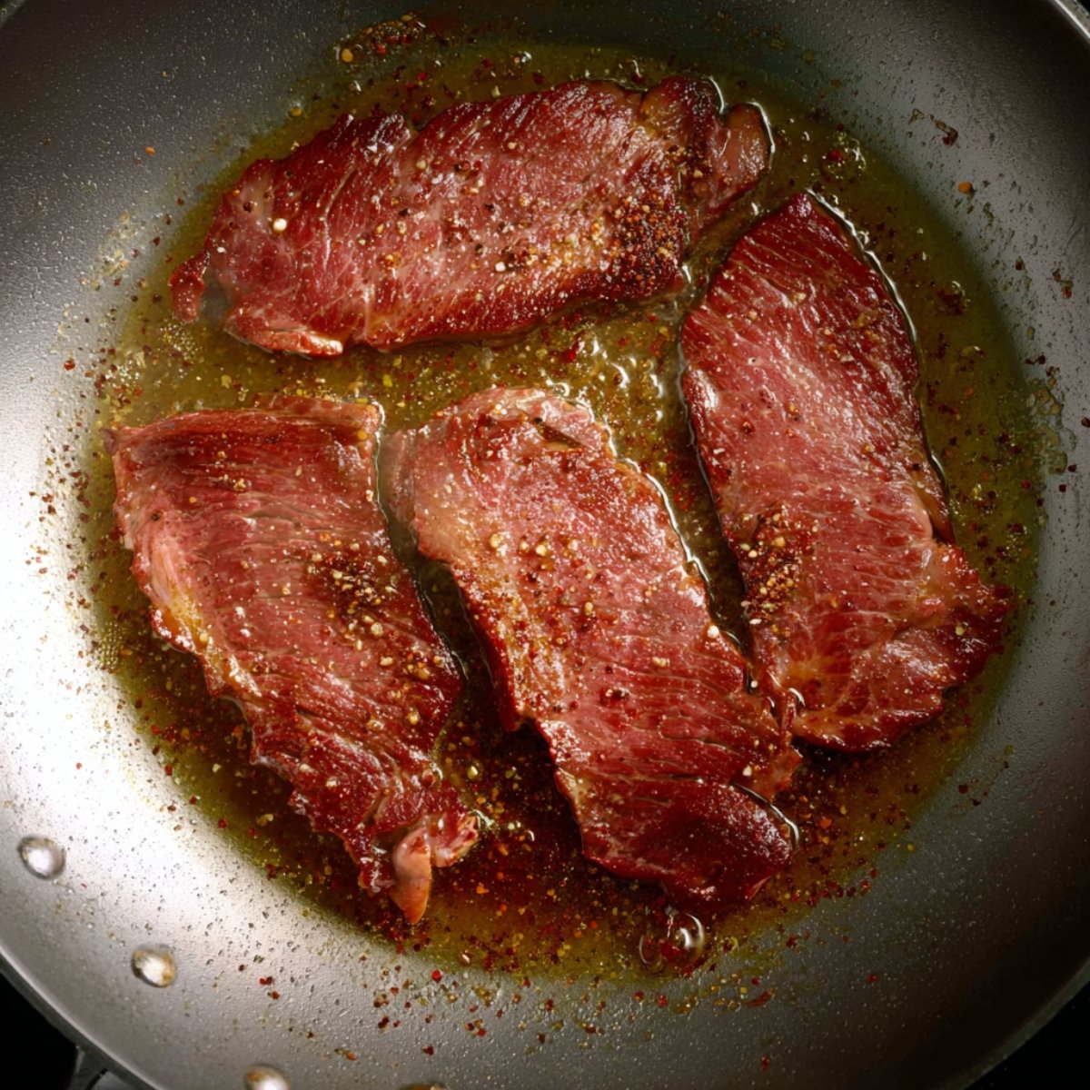 Crispy bacon strips frying in a skillet with oil and seasoning.