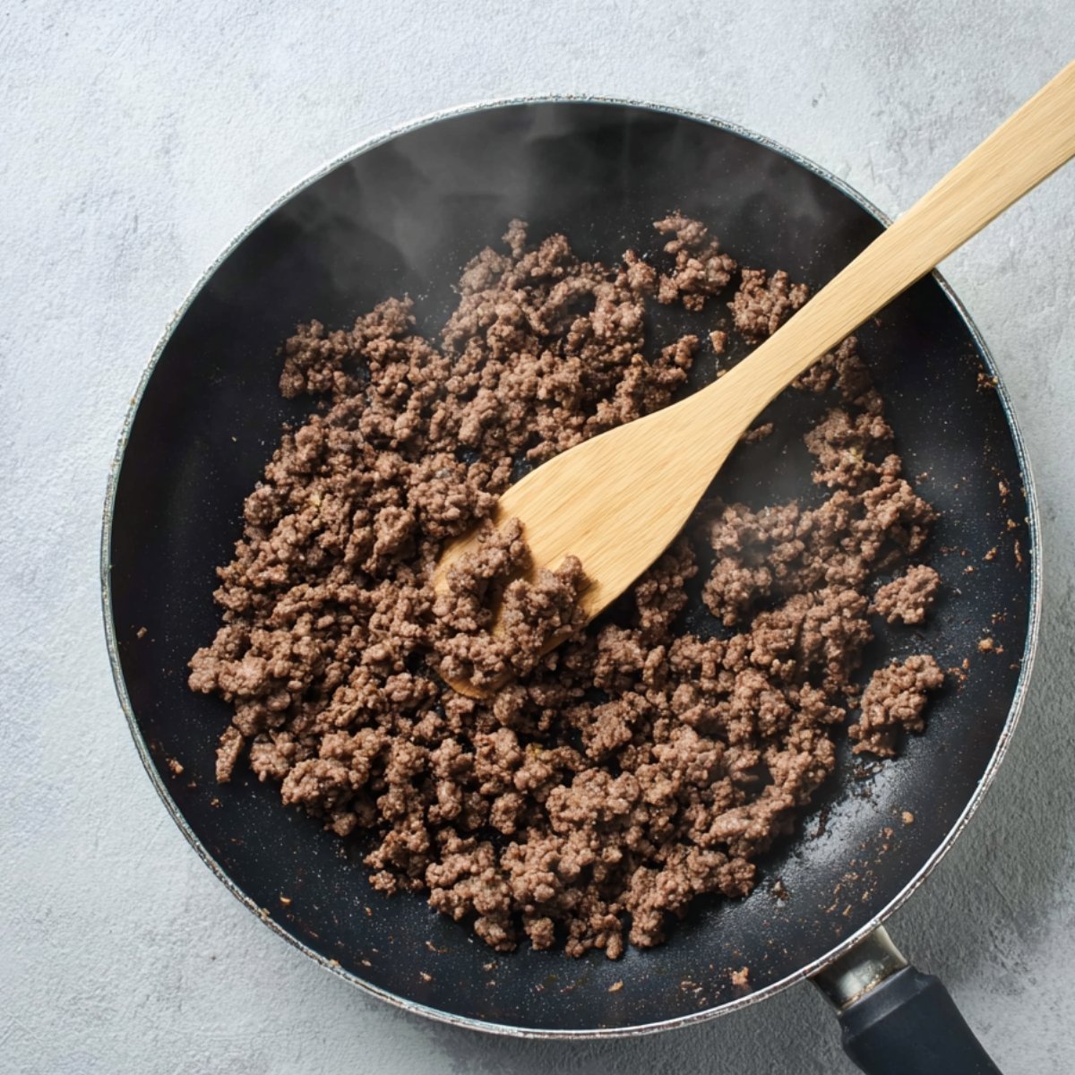 Pan-frying ground beef in a black skillet for cheeseburger quesadillas.