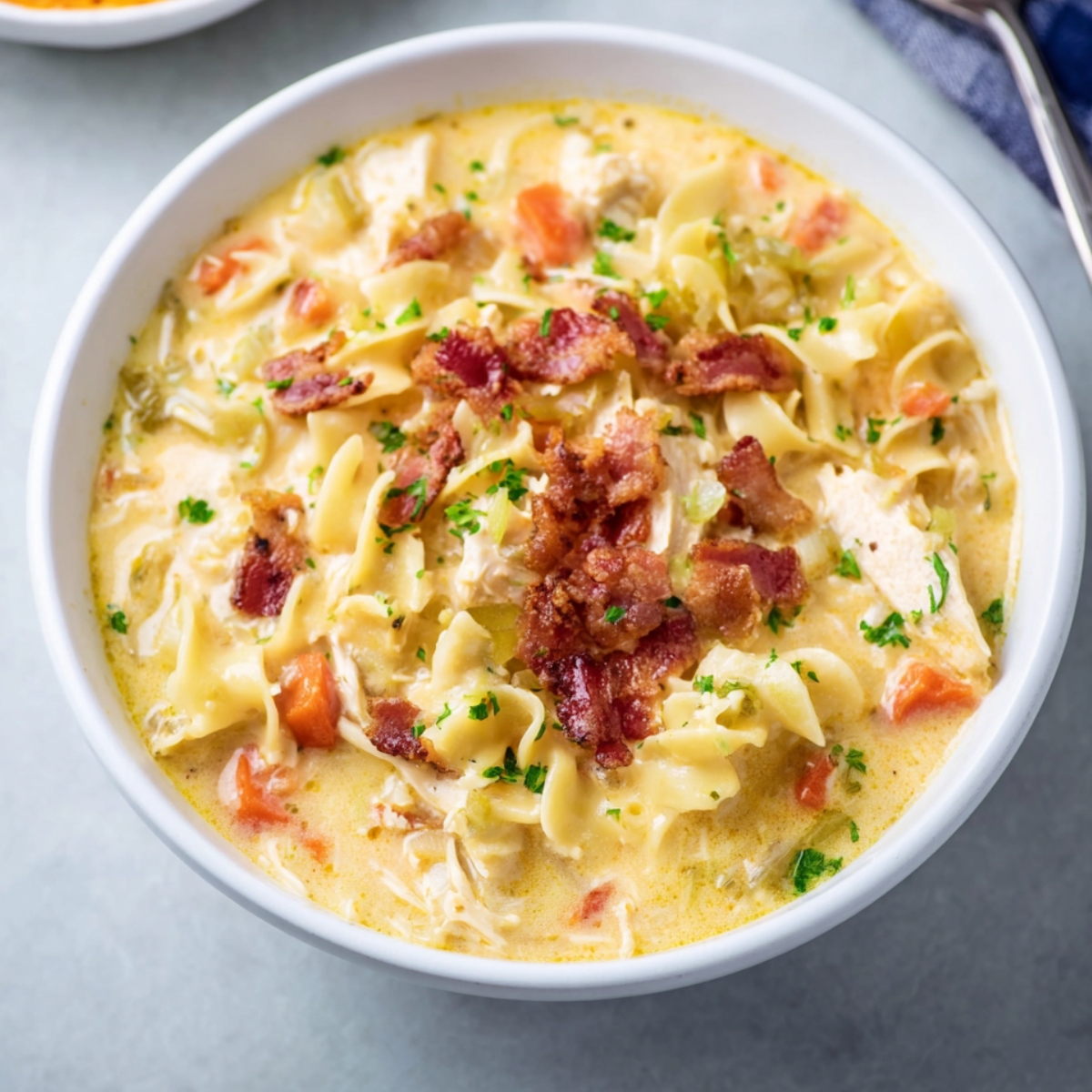 Creamy Crack Chicken Noodle Soup topped with crispy bacon in a white bowl