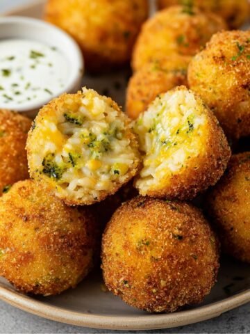 A close-up of Fried Rice Balls with a crispy breading and gooey cheese filling, served with dipping sauce.