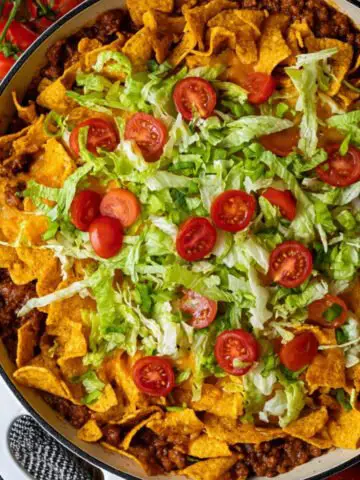 Frito taco casserole in a skillet topped with crushed Fritos, shredded lettuce, and cherry tomatoes, ready to serve