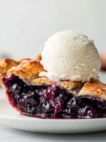 Close-up of blueberry pie slice with flaky crust and melting vanilla ice cream on top