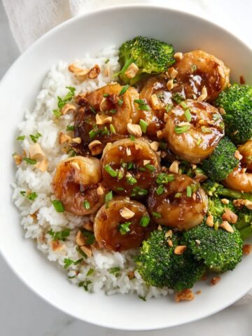 Honey Garlic Shrimp over white rice in a bowl, topped with chopped peanuts and fresh herbs, showing the glossy caramelized sauce.