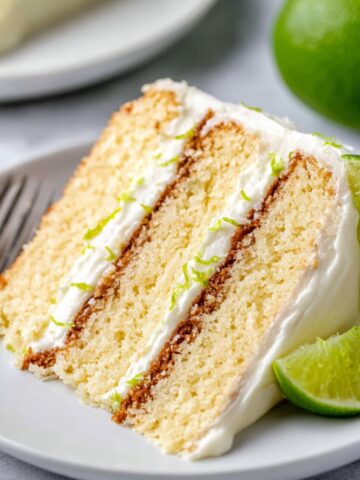 A slice of key lime cake on a plate, garnished with lime slices and frosting.