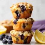 Stack of Lemon Blueberry Muffins Recipe with crumb topping, fresh blueberries and lemon on the side