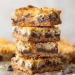 Stack of golden-baked Magic Cookie Bars with visible layers of chocolate chips, coconut, and a graham cracker crust.