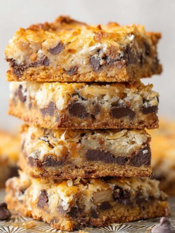 Stack of golden-baked Magic Cookie Bars with visible layers of chocolate chips, coconut, and a graham cracker crust.