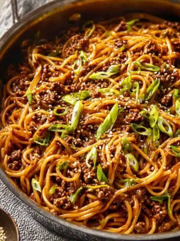 A skillet filled with Mongolian Ground Beef Noodles topped with green onions and sesame seeds, ready to be served.