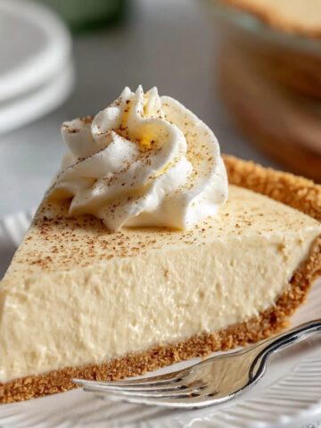 Slice of No Bake Eggnog Pie with graham cracker crust topped with whipped cream and nutmeg on a white plate