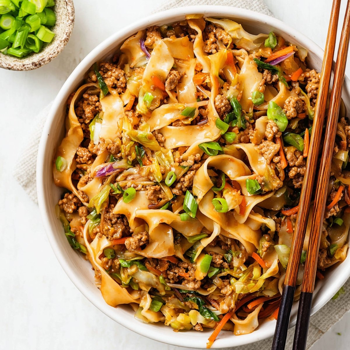 Potsticker Noodle Bowl with ground pork, cabbage, and wide noodles garnished with green onions and served with chopsticks