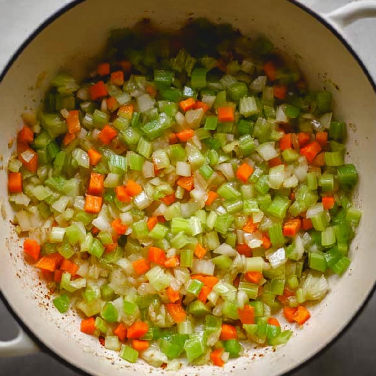Sautéed diced celery, carrots, and onions cooking in a large pot for soup base