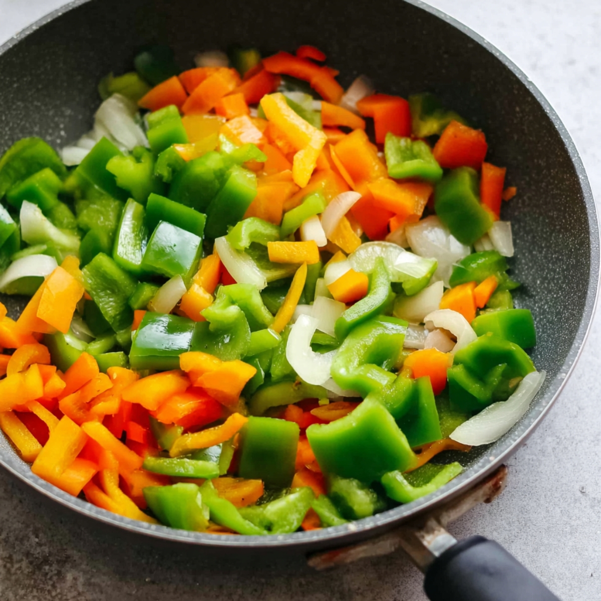 Chopped green, orange, and red bell peppers and onions sautéing in a pan.