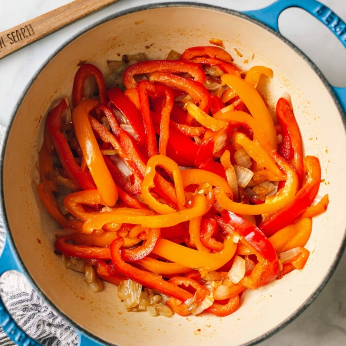 Sautéed red and orange bell peppers with onions cooking in a large pan for Cajun chicken pasta.