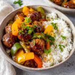 Sweet and sour meatballs served with colorful peppers, garnished with fresh parsley on a bed of rice.