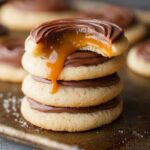 A tray of Twix Cookie Recipe with a visible bite taken from the top, revealing layers of caramel and chocolate with the cookie's soft interior.