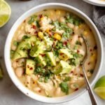 Bowl of white bean chicken chili topped with avocado, cilantro, and red pepper flakes, served with lime on the side.