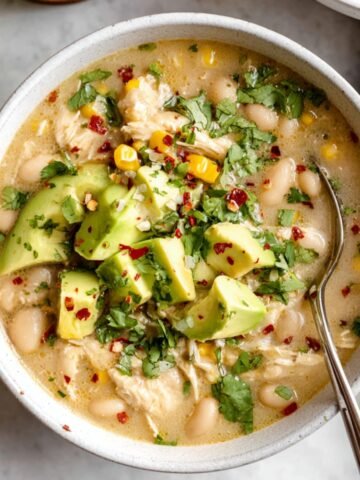 Bowl of white bean chicken chili topped with avocado, cilantro, and red pepper flakes, served with lime on the side.