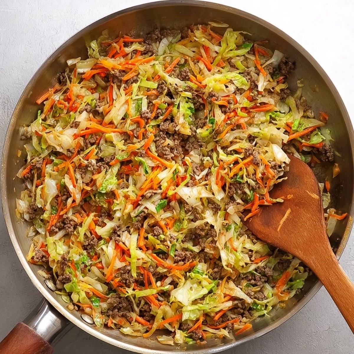 A skillet with sautéed ground beef and cabbage, mixed with carrots, creating a savory stir-fry dish. The vegetables are tender and have absorbed the rich flavors of the beef.