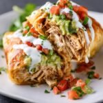 Baked Chicken Chimichangas, with shredded chicken filling and topped with sour cream, guacamole, and fresh diced tomatoes.
