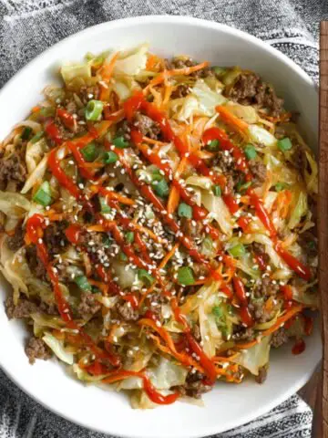 A finished bowl of Beef and Cabbage Stir Fry, topped with green onions, sesame seeds, and a drizzle of sriracha sauce for a flavorful, spicy kick.